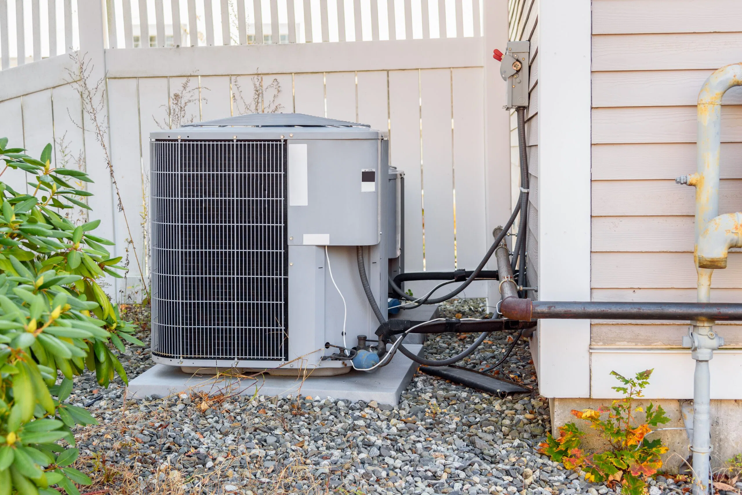 Hvac system exterrnal unit by a wooden fence in a house backyard